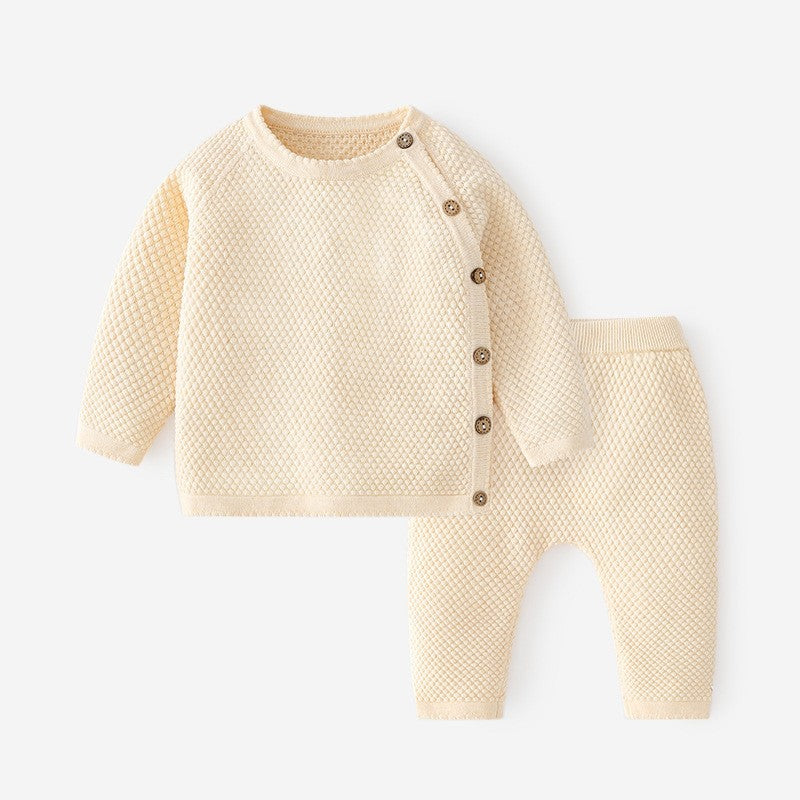 A beige knitted baby onesie with a round neckline and buttons down the front, paired with matching elastic waist pants.