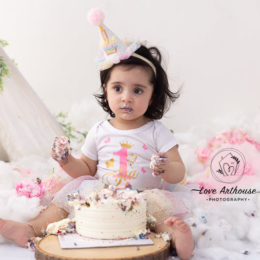 Baby celebrating a first birthday with a small cake, surrounded by flowers and a white background.