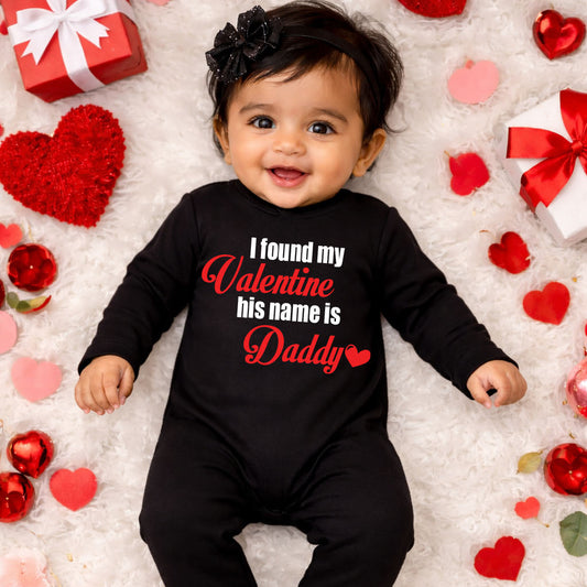 Baby wearing a black onesie with 'I found my Valentine his name is Daddy' text, surrounded by red and pink hearts and gift boxes.