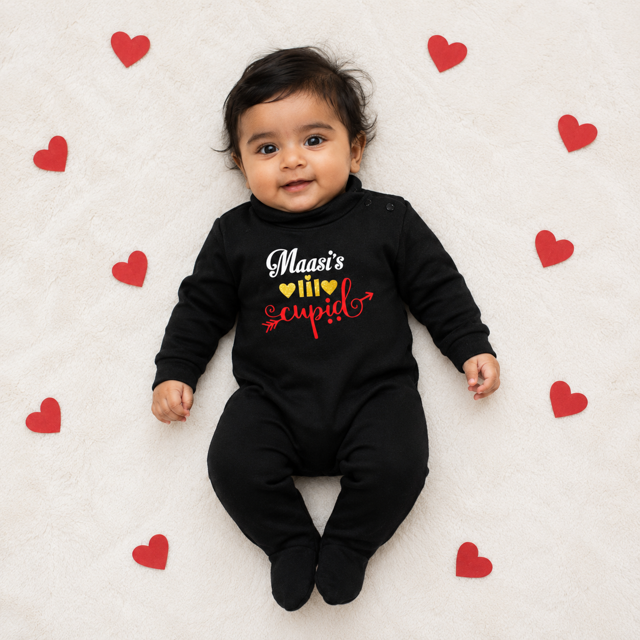 Baby wearing a black outfit with colorful text, surrounded by red hearts on a white background