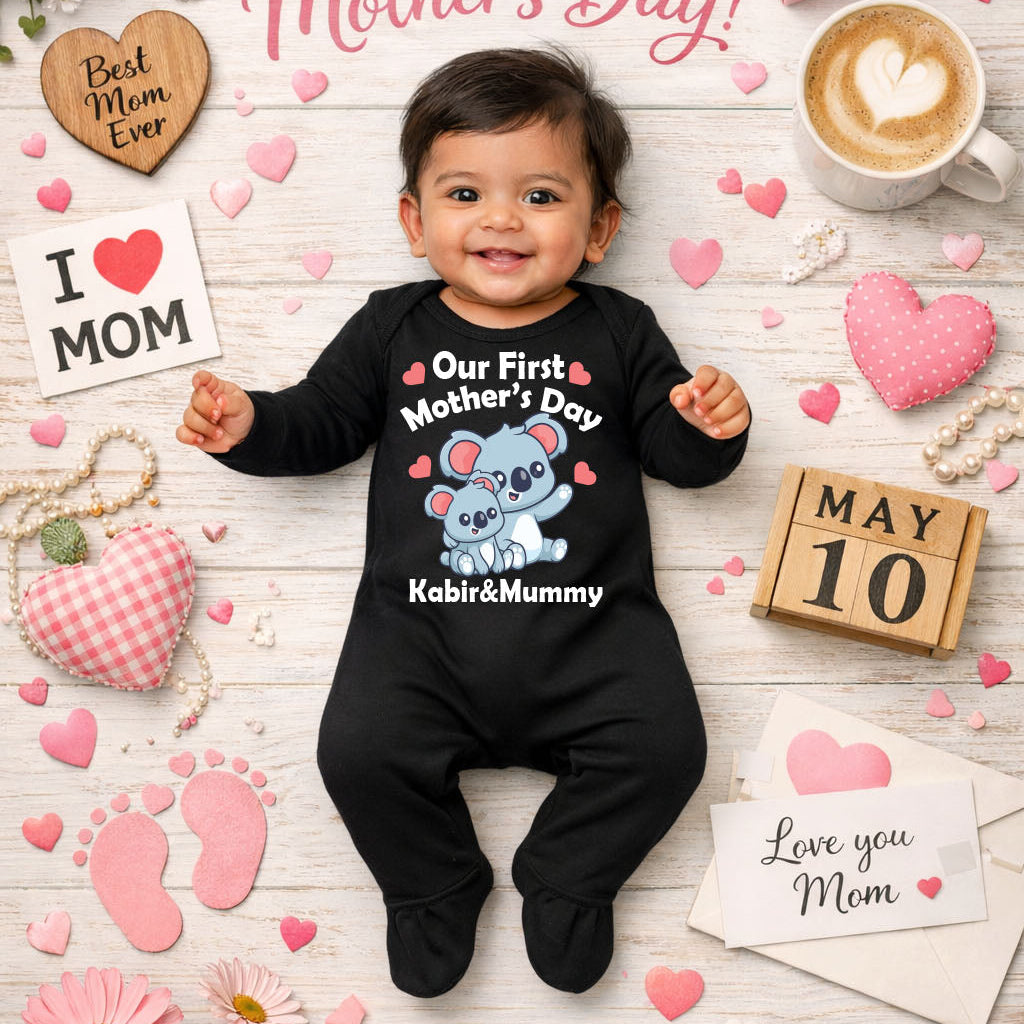 Baby wearing a 'Our First Mother's Day' shirt surrounded by Mother's Day decorations on a wooden floor.