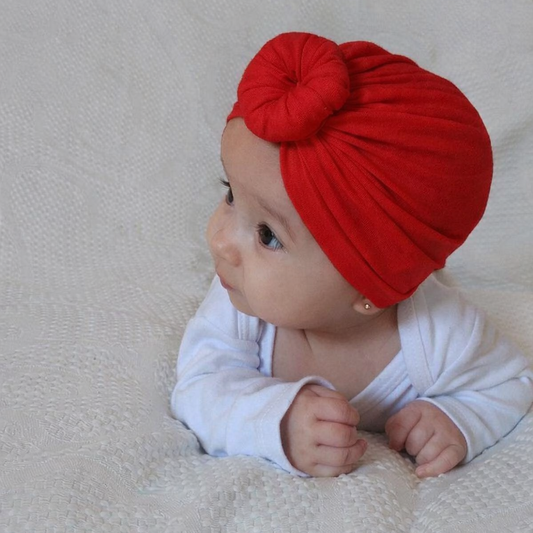 Baby wearing a red turban on a beige blanket