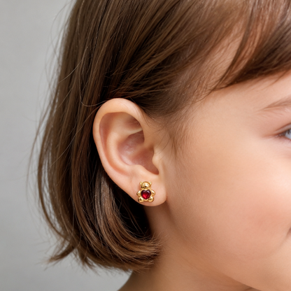 A close-up of a young child wearing a small gold stud earring with a red gemstone, shown in profile against a soft gray background.