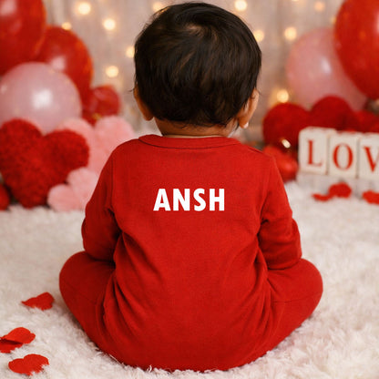 Child wearing a red outfit with 'ANSH' on it, sitting in a decorated room with balloons and heart shapes.