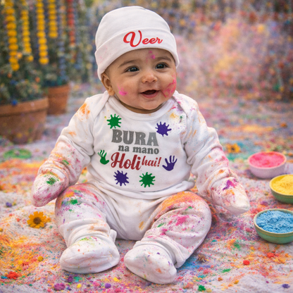 Baby in a colorful setting with Holi powder, wearing a onesie with text and a cap.