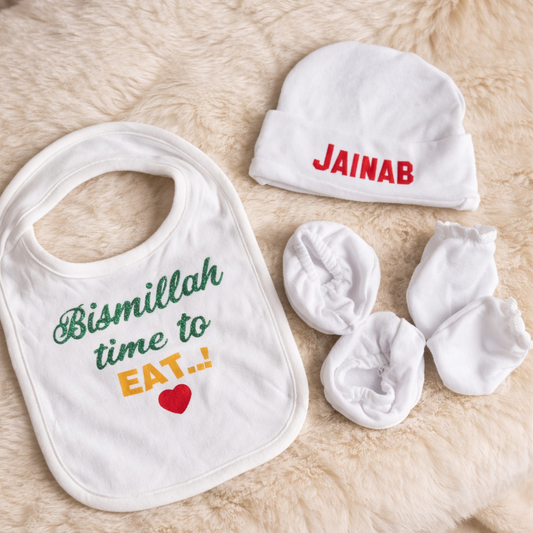 Baby bib, hat, and booties with personalized name on a soft surface