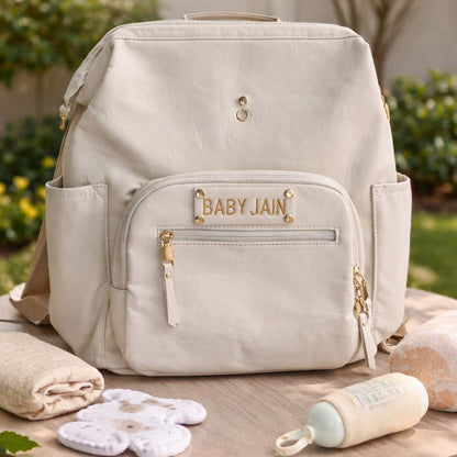 Beige backpack with 'Baby Jain' branding on a wooden table outdoors.