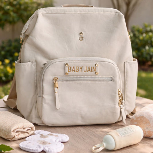 Beige backpack with 'Baby Jain' branding on a wooden table outdoors.