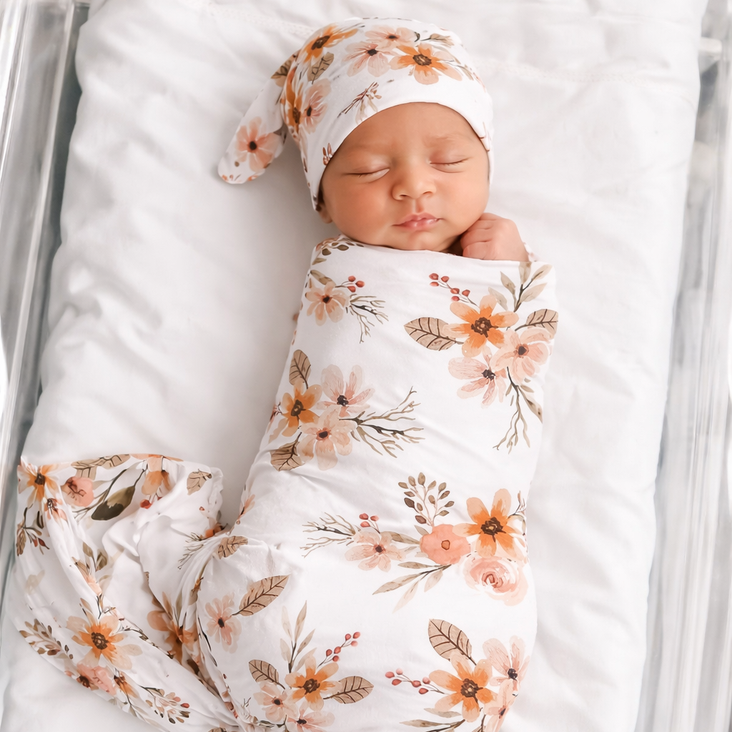 Newborn baby wrapped in a floral swaddle and headband, lying on a white blanket.