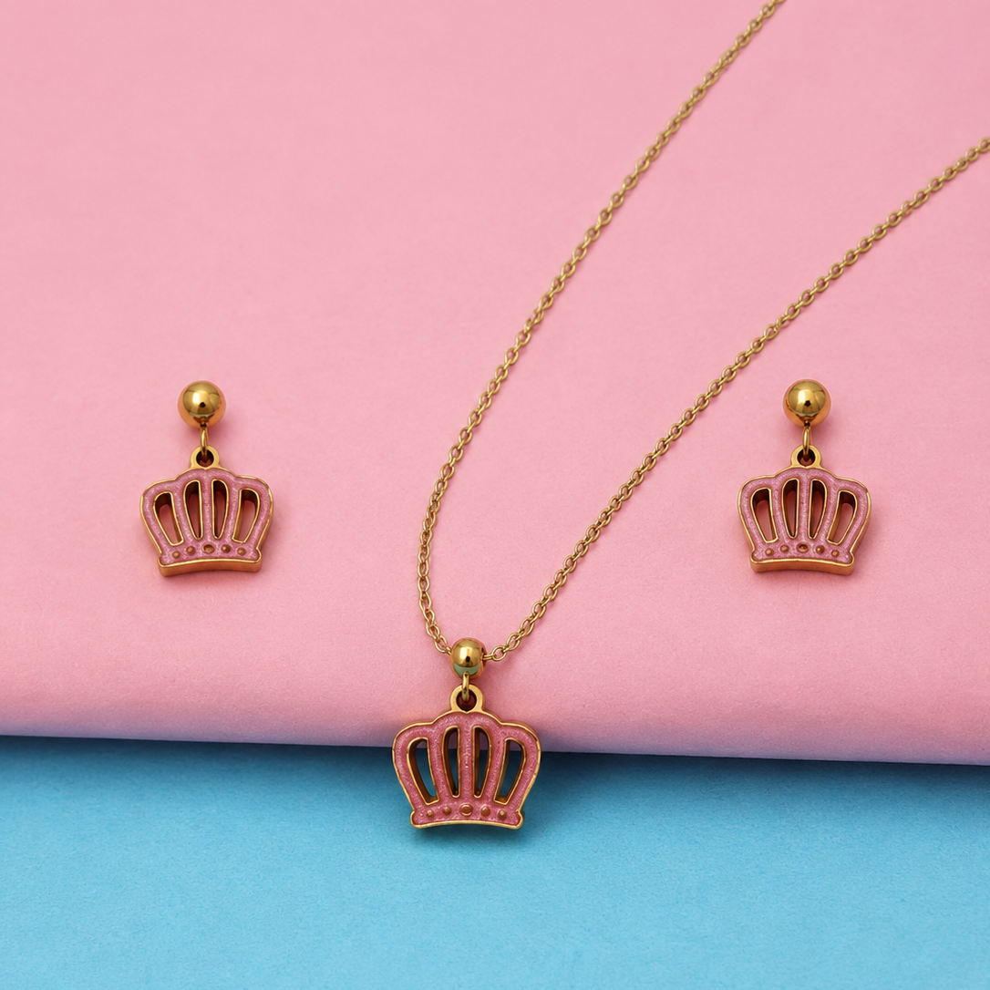 A gold crown pendant necklace and matching drop earrings with pink enamel detailing, displayed on a pink and blue background.