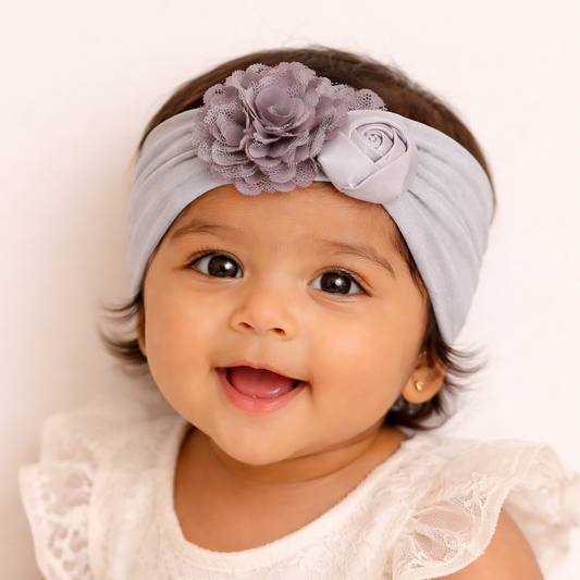Baby wearing a light gray headband with a flower, smiling against a white background