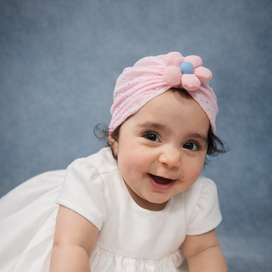Baby wearing a white dress and pink headband with a bow on a gray background