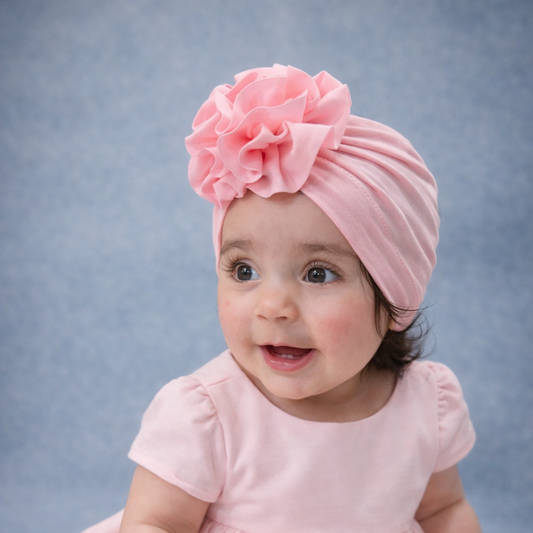 Baby wearing a pink dress and headband with a large flower on a gray background